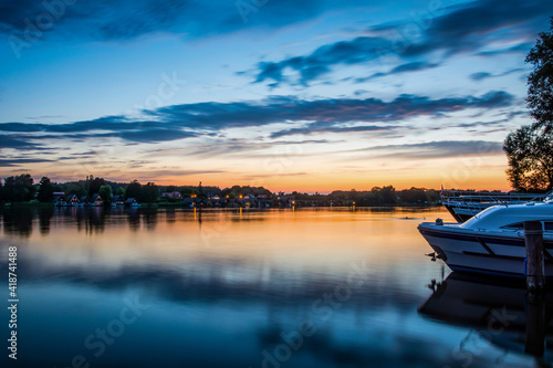 Peaceful sunset with dramatic sky and boats and a jetty. Tranquil Scene at dusk on a lake on a summer day