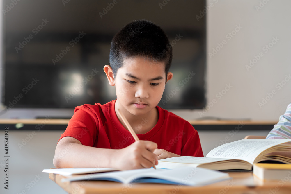Image of a young Asian boy taking notes from studying in the classroom Image of a young Asian boy taking notes from studying in the classroom
