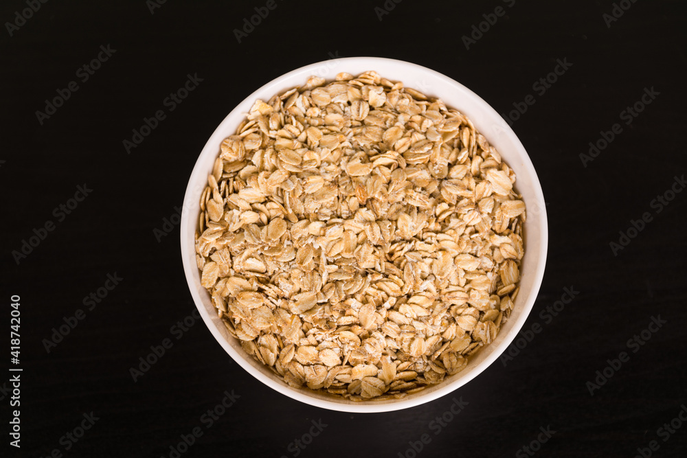 Pile of oats in round white bowl on black table top view Pile of oats in round white bowl on black table top view