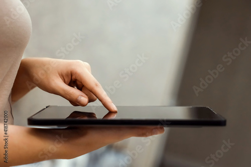 A female hand presses on the screen of a digital tablet close-up, side view. New technology concept, multimedia.