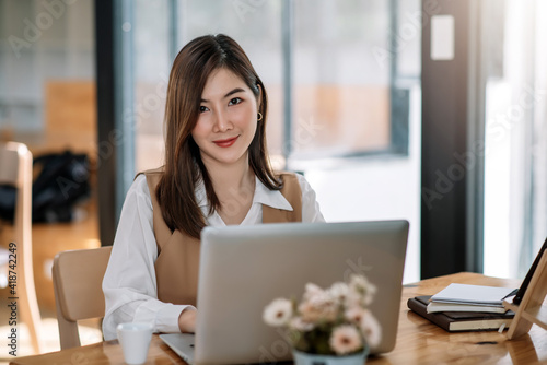 Charming Asian woman working at the office using a laptop Looking at the camera.