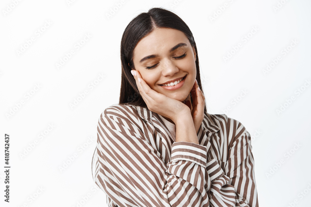 Tenderness and beauty. Portrait of young woman feeling happy about her facial skin, taking care of face, close eyes and smiling romantic, standing against white background Tenderness and beauty. Portrait of young woman feeling happy about her facial skin, taking care of face, close eyes and smiling romantic, standing against white background