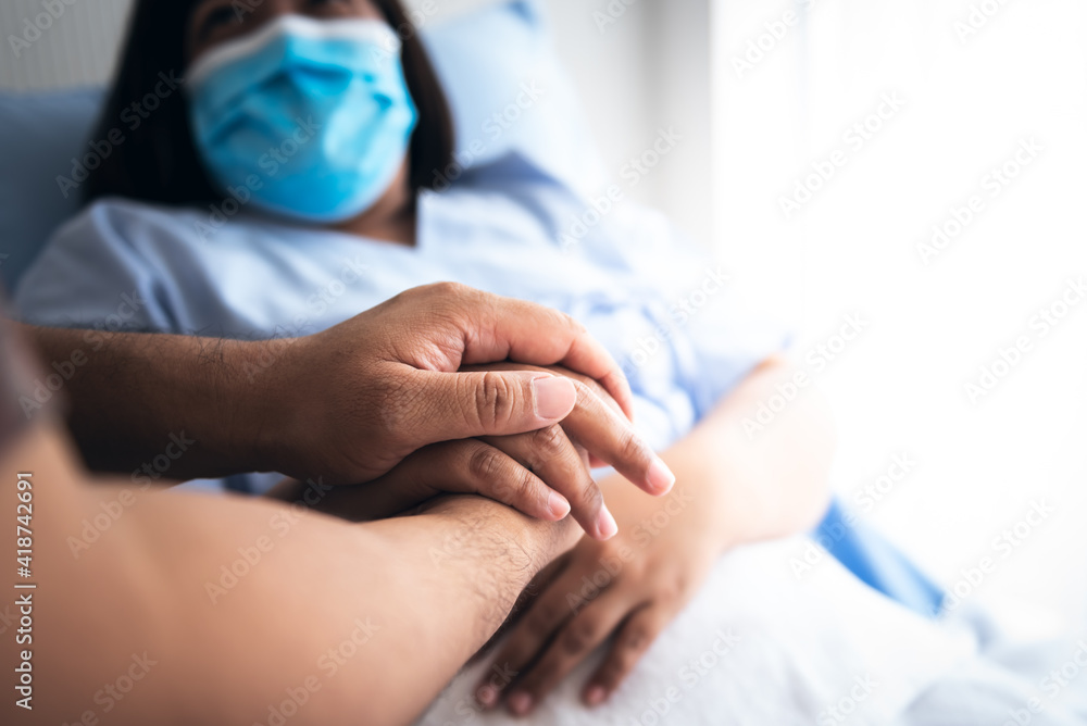 The people hold hands woman patient Which wearing a surgical mask and lying in the patient's bed, to encourage To fight the disease, cheer to receive treatment, to people and health care concept.