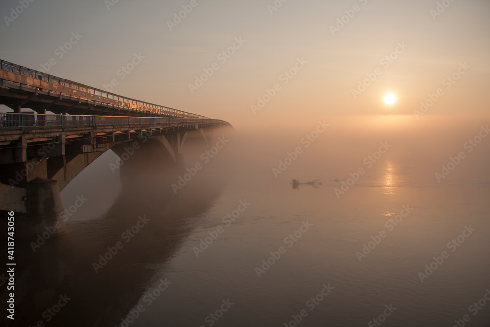 Fototapeta premium Sunrise over the spring river. A bridge over a large river.. Fog on the river in early spring