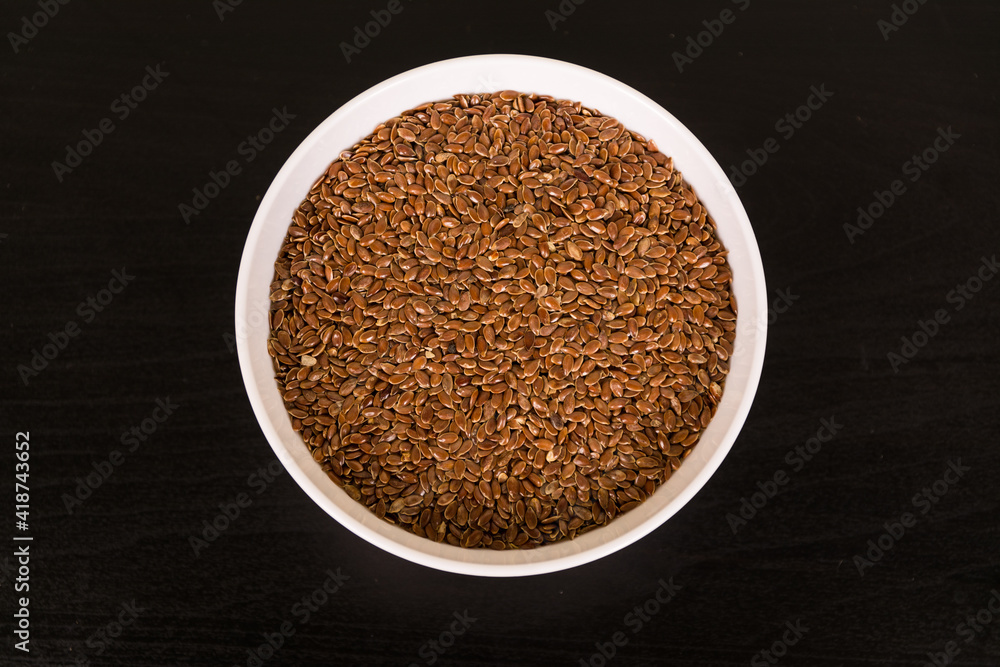 pile of Flax seeds in round white bowl on black table top view pile of Flax seeds in round white bowl on black table top view