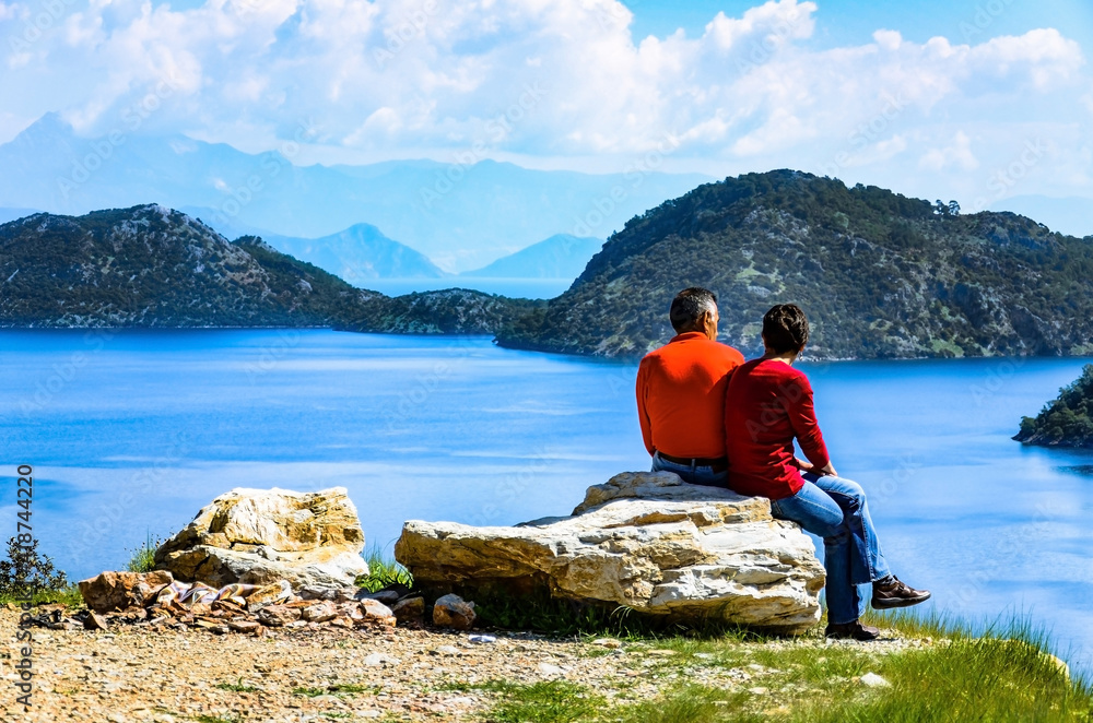 A couple sitting on a big rock and enjoying the view of the blue waters of the Mediterranean sea laying before them