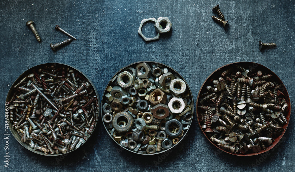 Various old nuts and screws in round tin cans, close up, stylized