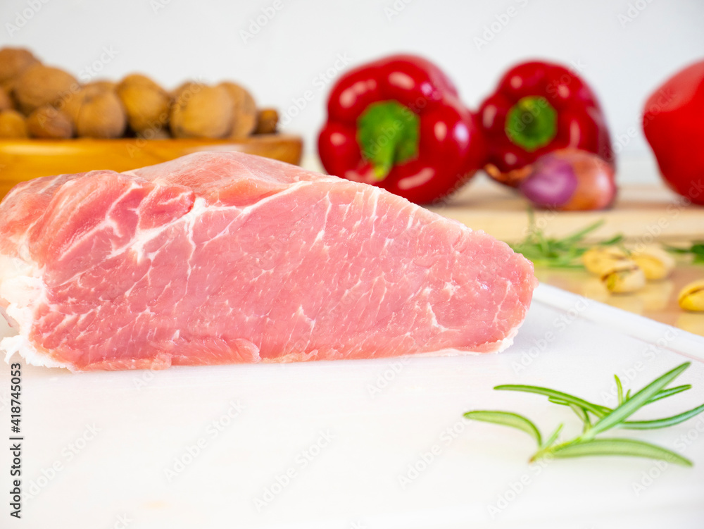 Cut Piece of Pork Loin on white cutting board, raw fresh meat on kitchen table with various ingredients and spices Cut Piece of Pork Loin on white cutting board, raw fresh meat on kitchen table with various ingredients and spices