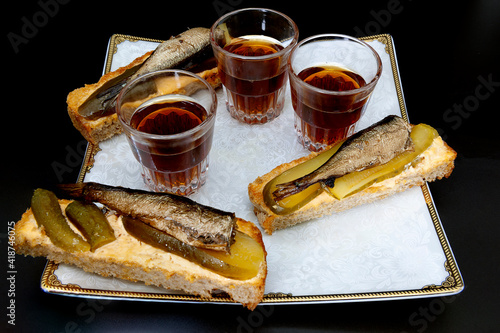 three sandwiches made of bread, butter, pickled cucumbers and Baltic sprats, three glasses with alcohol