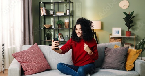 Portrait of relaxed Caucasian millennial pretty woman hold smartphone watching social media stories video sitting on sofa in living room. Happy young lady using mobile apps resting at home