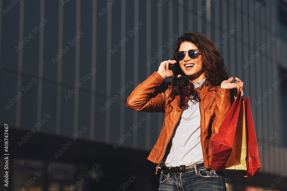 Φωτογραφία Happy young woman with shopping bags talking on the phone on street