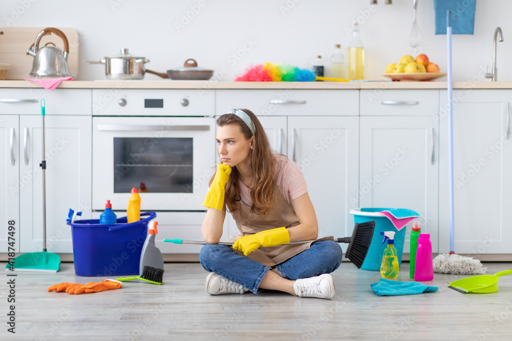 Φωτογραφία Unhappy millennial housemaid sitting on kitchen floor with heaps of supplies, si