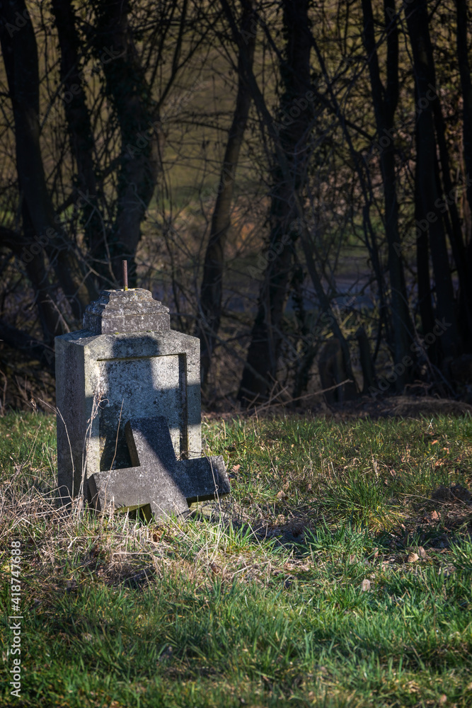Old tombstone with broken cross but with a shadow in cross shape under trees in an abandoned cemetery, religious symbol, copy space Old tombstone with broken cross but with a shadow in cross shape under trees in an abandoned cemetery, religious symbol, copy space