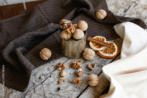 Walnuts in a tin of yellow metal next to the shell and the nuts on the inside. Decorated with dried oranges and a cinnamon stick. Composition of products and food on a wooden Board