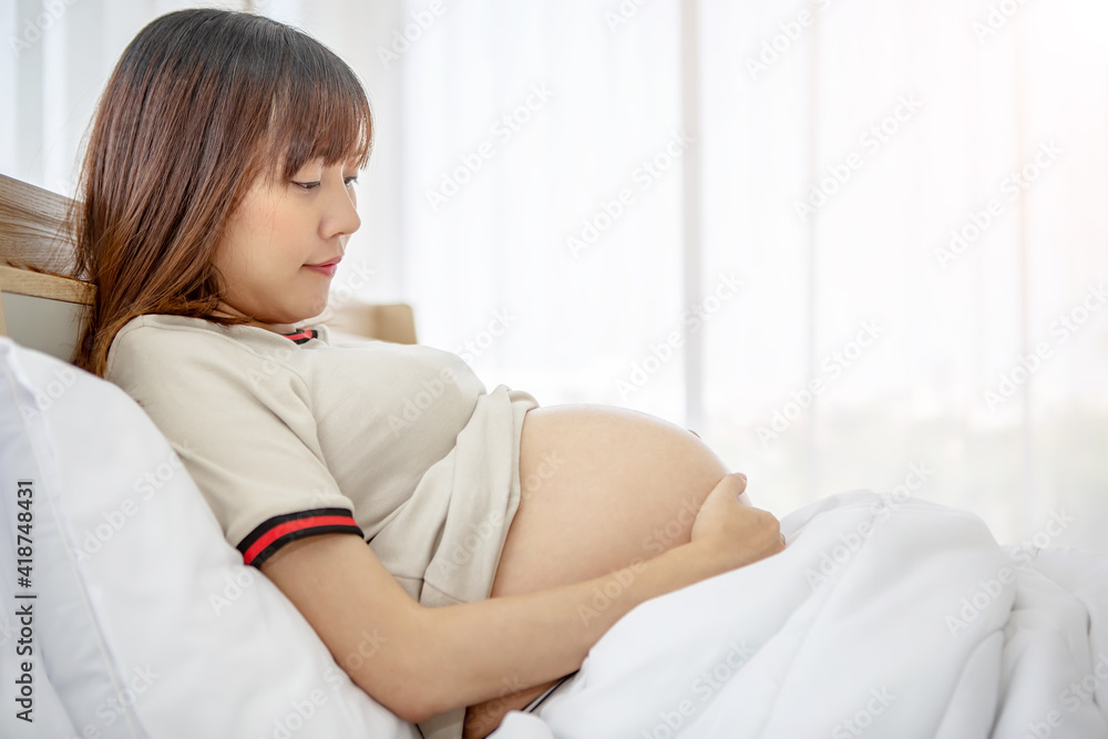 Pregnant woman taking care of her child by holding baby in her pregnant belly in the bedroom Pregnant woman taking care of her child by holding baby in her pregnant belly in the bedroom