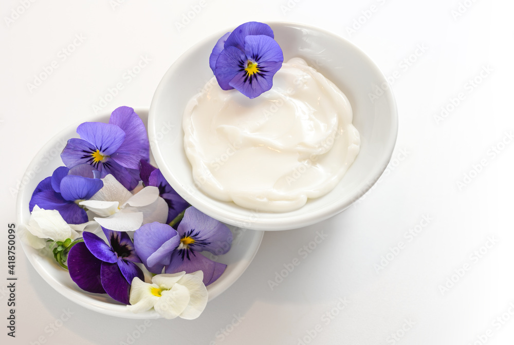 Natural balm from viola or violet flowers in white bowls, cosmetics concept, white gray background with copy space, selected focus Natural balm from viola or violet flowers in white bowls, cosmetics concept, white gray background with copy space, selected focus