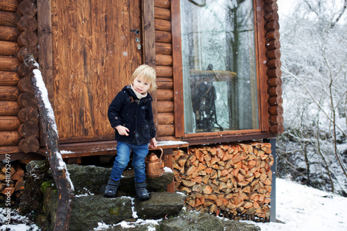 Cute toddler child in a little fancy wooden cottage, sitting on the front porch with a pot of tea photo