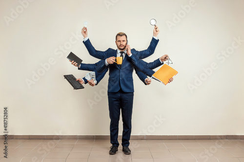 Businessman with many hands in a suit. Works simultaneously with several objects, a mug, a magnifying glass, papers, a contract, a telephone. Multitasking, efficient business worker concept. photo