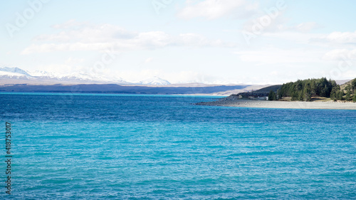 Lake Tekapo with nearby snow covered mountain peaks on a sunny day in the South Island of New Zealand.