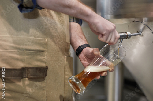 Close up of male brewmaster pouring craft beer into glass from tap at brewing factory, copy space