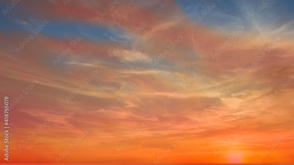 Colorful sunset during golden hour with pastel colors and white clouds.  Some of the blue sky is visible. 