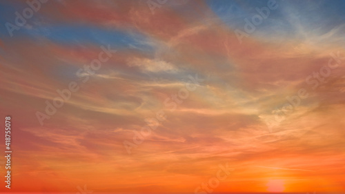 Colorful sunset during golden hour with pastel colors and white clouds. Some of the blue sky is visible. 