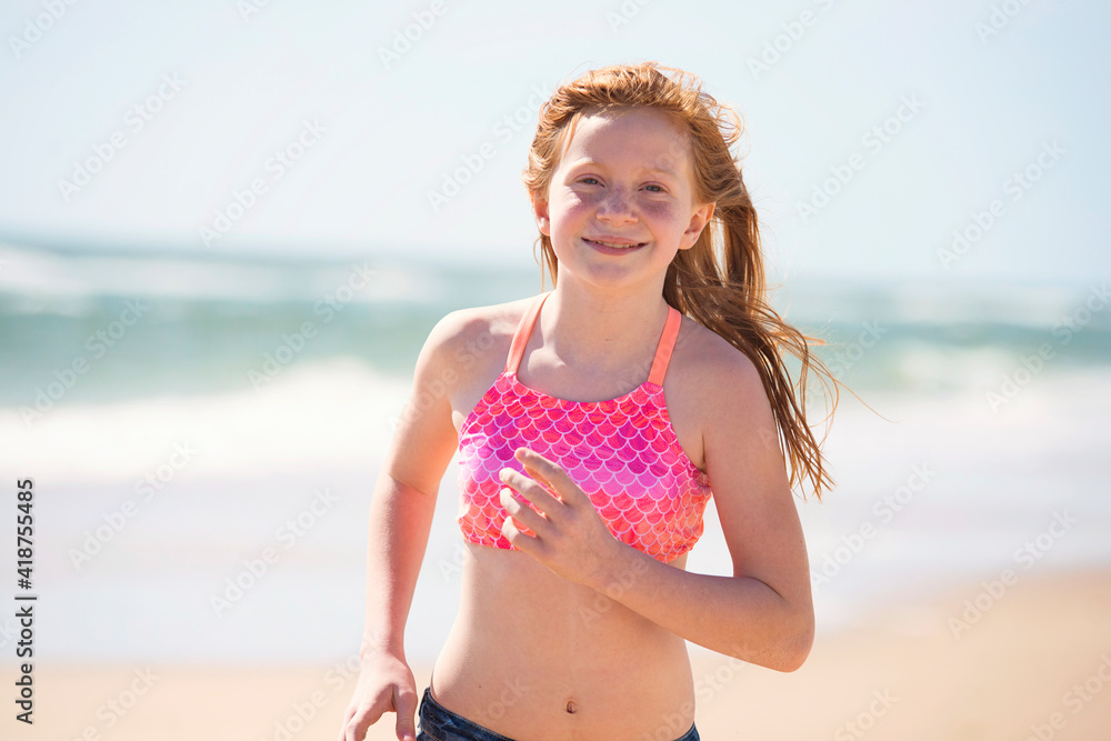 Tween red haired girl in swimsuit running by the ocean. Stock Photo