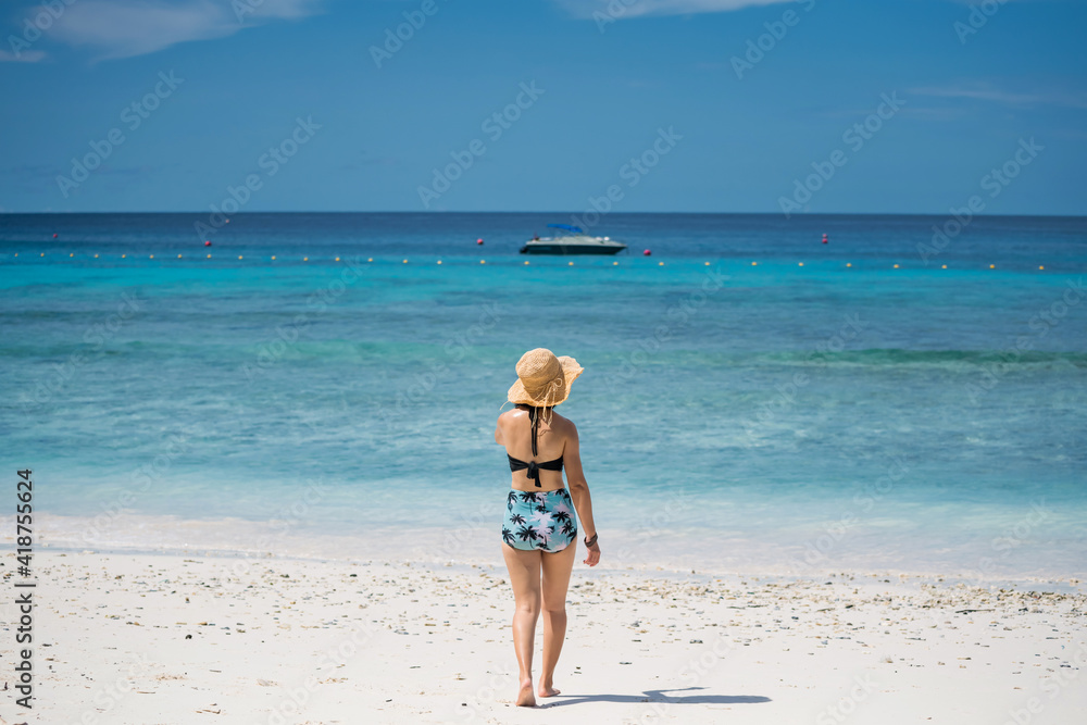 Rear of young Asian girl with bikini and hat on white sand beach walking to turquoise andaman sea at Similan island, Phang Nga, Thailand. Holiday maker or vacation in tropical country. summer concept.