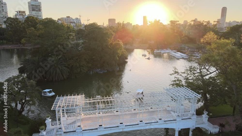 Aerial dolly in over white bridge and boats sailing in pond at Rosedal gardens at golden hour, Buenos Aires photo