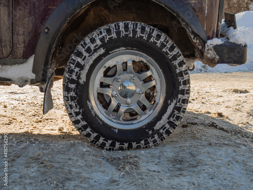 A wheel with a beautiful SUV car disc. Winter studded tires on off road. The concept of winter car competitions on ice. The texture of a rubber tire with spikes in the snow.