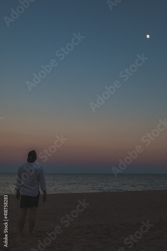 man standing at sea beach looking at moon