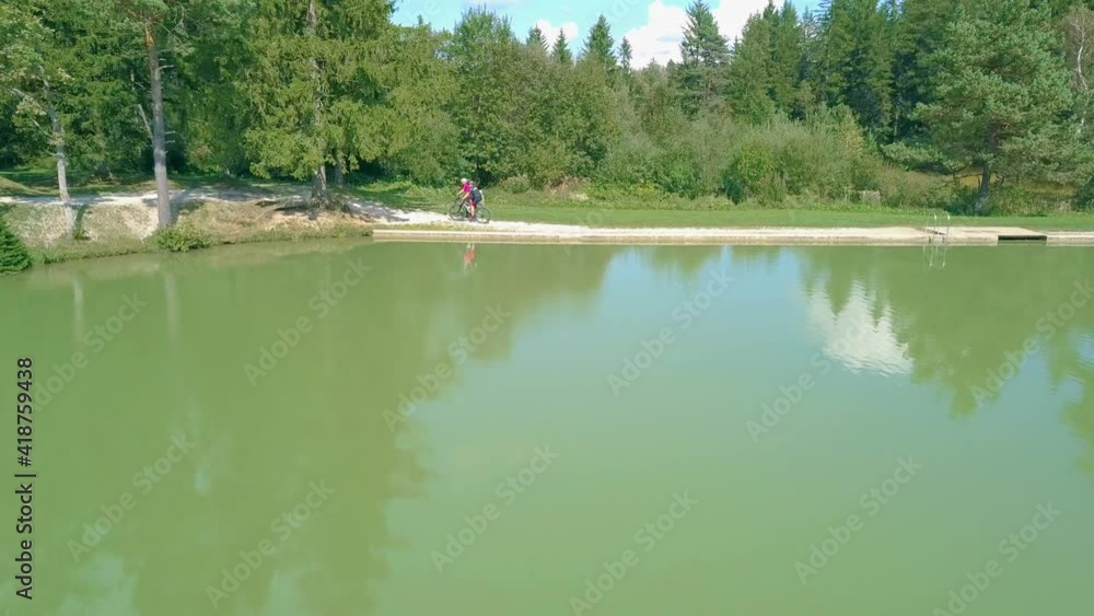 Aerial View Of Couple Cycling Along Path Next To Outdoor Pool. Dolly Left Aerial View Of Couple Cycling Along Path Next To Outdoor Pool. Dolly Left