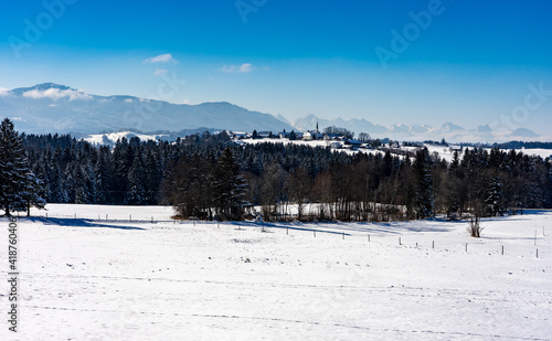 Winterwanderung mit Blick auf die Ammergauer und Allgäuer Alpen: Das Dorf Schönberg mit Kirchturm und Schneelandschaft © Frank Lambert