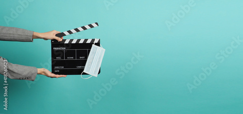 Hands with grey suit and hold black Clapper board or movie slate with face mask. it use in video production ,movies and cinema industry on blue and green or mint background.