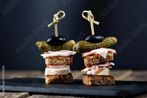 canapes slices of black bread cream bacon pickled cucumbers of olive on a stud on a black shale stand on a black background