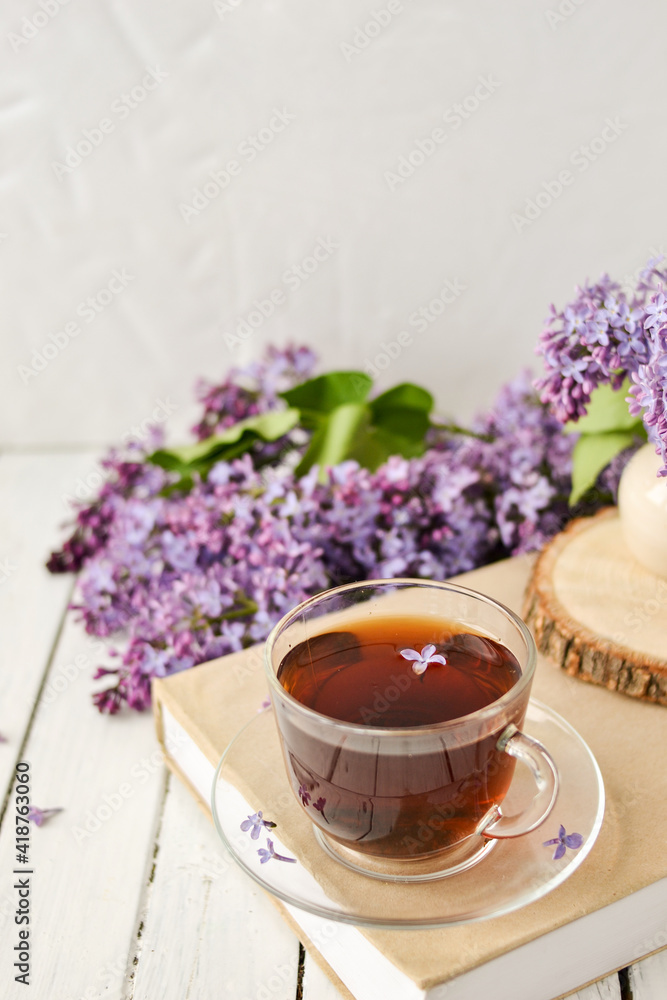 Romantic background with a cup of tea, lilac flowers and a book over a white wooden table. Leisure concept, spring breakfast Romantic background with a cup of tea, lilac flowers and a book over a white wooden table. Leisure concept, spring breakfast