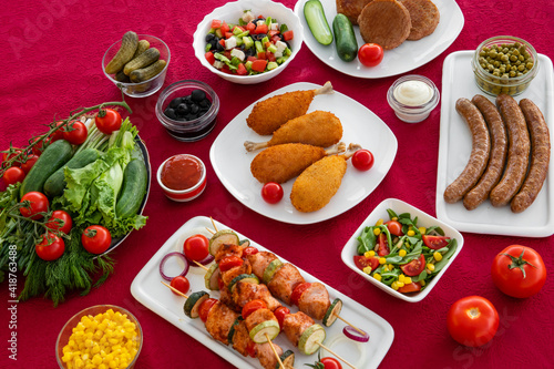 Delicious homemade dinner. Sausages with fresh vegetables, kebab with grilled vegetables, cutlet with fresh salad. White plate on red background.
