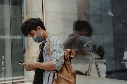 Asian man wearing surgical face mask using smart phone in outdoor.