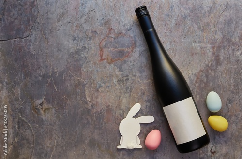 Top view of wine bottle with blank label and Easter eggs and white bunny on dark stone table background. Wine bottle mockup. Copy space for text.