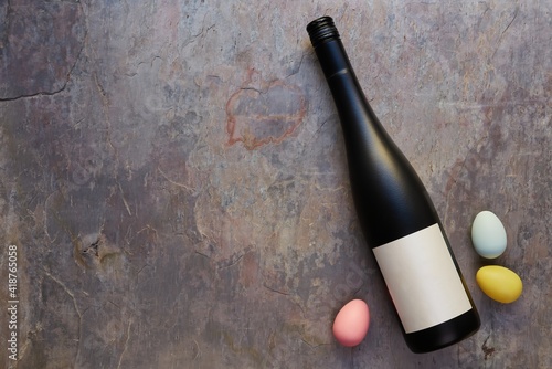 Top view of wine bottle with blank label, and colorful Easter eggs on table. Wine bottle mockup. Copy space.