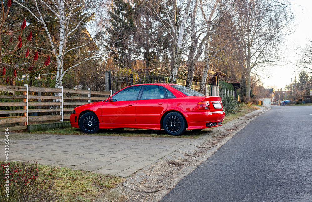 Fototapeta premium Beautiful red car parked on rural street near fence