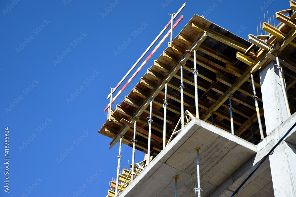 concrete structure frame. building construction site. steel and wood formwork. scaffolding. beams and plywood sheathing. striped wooden safety barrier. perspective view. clue sky. copy space.