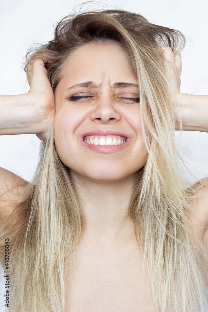 A beautiful young caucasian blonde woman holds her head and covers her ears with her hands. Despair, frustration, headache, migraine, exhaustion, emotional breakdown, voices in the head, fear A beautiful young caucasian blonde woman holds her head and covers her ears with her hands. Despair, frustration, headache, migraine, exhaustion, emotional breakdown, voices in the head, fear