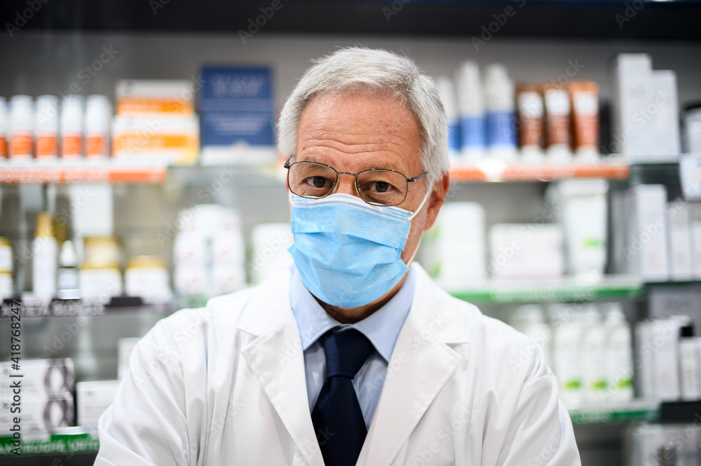 Senior pharmacist wearing a mask due to coronavirus pandemic in his store Senior pharmacist wearing a mask due to coronavirus pandemic in his store