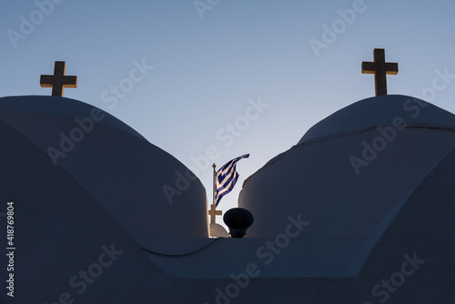 Close up of the Taxiarhis church's domes in Vathy beach, Sifnos island, with the windy Greek flag between two crosses during sunset. Cyclades. Greece. photo