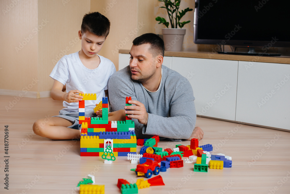 Fototapeta premium A little boy together with his father is played by a constructor and builds a house. Construction of a family home.