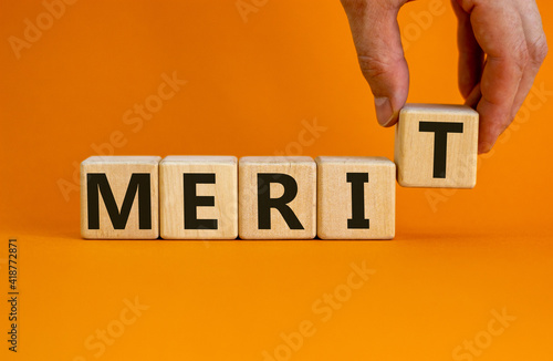 Merit symbol. Wooden cubes with the word 'merit'. Businessman hand. Beautiful orange background, copy space. Business and merit concept.