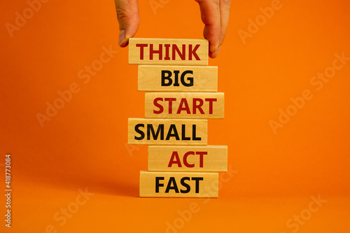 Think big start small symbol. Words 'Think big start small act fast' on wooden blocks on a beautiful orange background. Businessman hand. Business, motivational and think big start small concept. photo