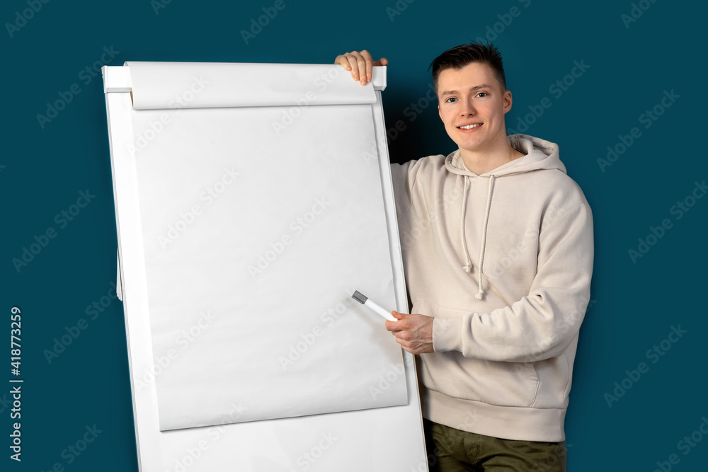 A young businessman stands near the whiteboard and makes a presentation. Blue background. Place for your text. High quality photo A young businessman stands near the whiteboard and makes a presentation. Blue background. Place for your text. High quality photo