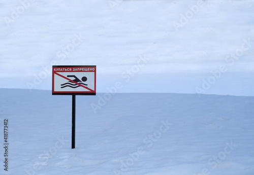 Winter, frost, snow. In a snowdrift, a sign with the inscription in Russian "swimming is prohibited".